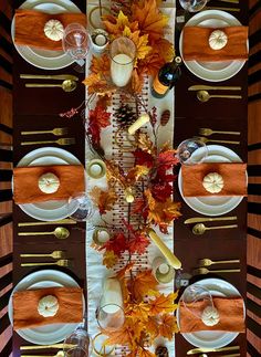 the table is set with white plates, silverware and autumn leaves on it's placemats