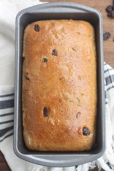 a loaf of bread sitting in a pan on top of a wooden table next to raisins