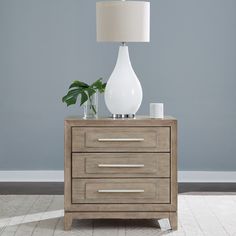 a white vase sitting on top of a wooden table next to a lamp and a potted plant