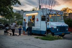 several people standing in front of an ice cream truck at sunset with the sun setting behind them