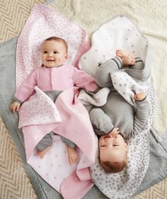 two babies laying next to each other on top of a blanket covered in pink and gray blankets