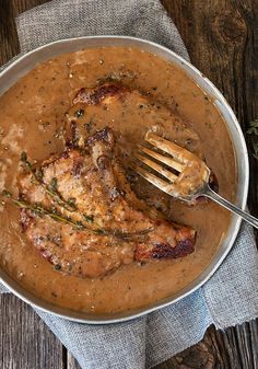 a pan filled with meat and gravy on top of a wooden table