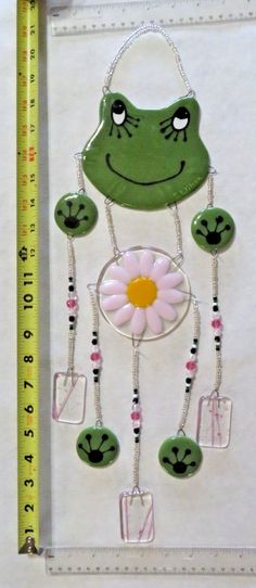 a green frog holding a pink flower next to a ruler