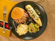 a black plate topped with food next to a fork and napkin on top of a table