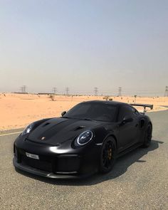 a black sports car parked on the side of a road in front of sand dunes