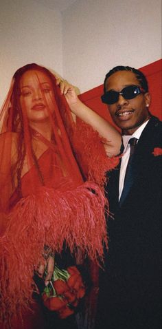 a man in a suit and sunglasses standing next to a woman wearing a red dress