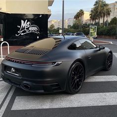 a grey sports car parked in front of a building with palm trees and buildings behind it