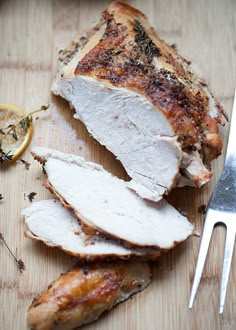 sliced up chicken on a cutting board with a knife and lemon wedges next to it