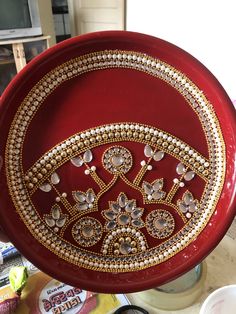 a red plate with gold and white designs on it sitting on a table next to other items