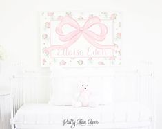 a white crib with a pink bow and name sign on the wall above it