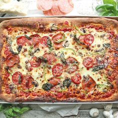 a pizza with tomatoes, cheese and spinach on it in a pan next to garlic