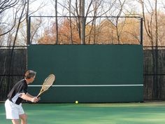 a man holding a tennis racquet on top of a tennis court with trees in the background