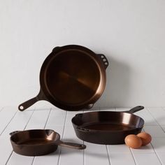 two pans and an egg on a white tile floor with a wall in the background