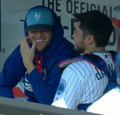 two baseball players sitting next to each other in the dugout at a ball game