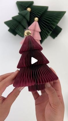 someone is holding up some origami christmas trees with ornaments on top of them