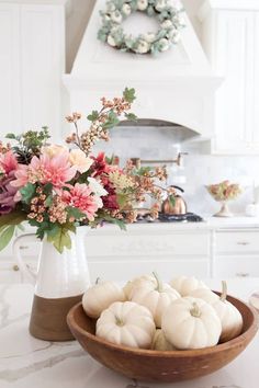 flowers and pumpkins in a bowl on a kitchen counter