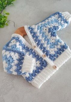 a blue and white crocheted sweater on a wooden hanger next to green leaves