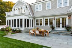 a patio with table and chairs in front of a large gray house on a sunny day