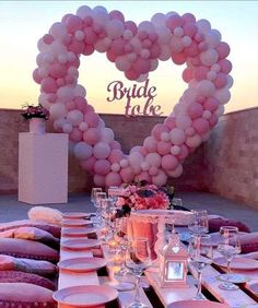 a table topped with lots of pink plates and glasses next to a heart shaped balloon