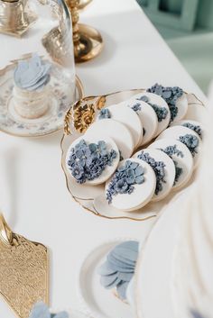 blue and white desserts are on a table with gold trimmed plates, silverware, and glass vases