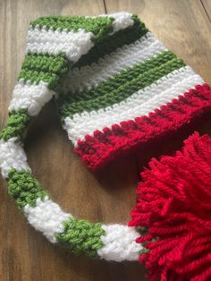 a crocheted hat sitting on top of a wooden floor next to a red and green pom pom