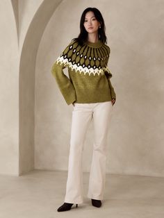 a woman standing in front of an arch wearing a green sweater and white pants