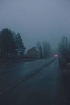 a foggy street with houses and trees in the distance on a gloomy day