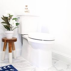 a white toilet sitting in a bathroom next to a wooden stool with flowers on it