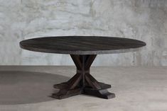 a round wooden table sitting on top of a cement floor next to a white wall