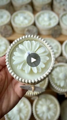 a person holding a small white flower in front of some cupcakes