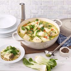 a large pot filled with food on top of a wooden cutting board next to white plates