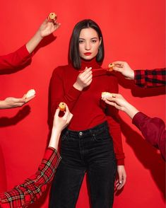 four people holding donuts in their hands while standing against a red background with one woman eating them