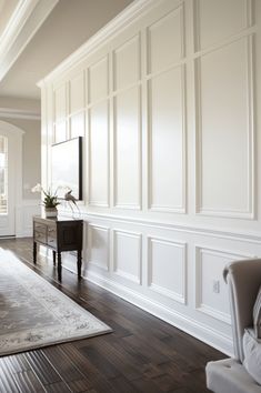 a living room with hard wood floors and white paneling on the walls, along with a large rug