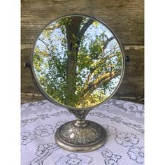 a round mirror sitting on top of a table next to a tree in the background