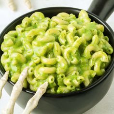 a black bowl filled with macaroni and cheese next to two white garlic sticks