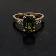 This is a very special one of a kind ring that is set in 14 karat yellow gold. The center stone is a Rare Natural Ceylon Green Sapphire with no indication of heat applied. This specialty mixed cut stone has a deep green tone with shades of soft yellow as well. The hardness on this stone is a 9 out of 10 on the Mohs scale. It weighs 3.25 carats and is surrounded by 6 Natural French Cut Square Diamonds weighing 0.26 carats total weight and the stones are graded G in color and VS2 in Clarity. These Green Princess Cut Diamond Ring In 14k Gold, 14k Gold Green Diamond Princess Cut Ring, Princess Cut Green Diamond Ring In 14k Gold, Timeless Green Rings With Accent Stones, Green Diamond Ring With Princess Cut And Accent Stones, Green 14k Gold Ring With Accent Stones, Green Princess Cut Diamond Ring With Accent Stones, 14k Gold Green Rings With Accent Stones, Green 14k Gold Rings With Accent Stones