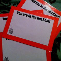 three red and white envelopes sitting on top of a camouflage print tablecloth with the words you are in the hot seat