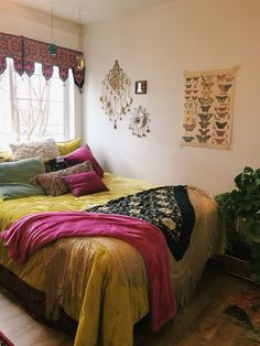 a bed sitting in a bedroom next to a window covered in blankets and throw pillows