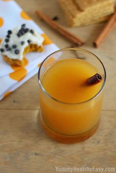 a glass filled with orange juice next to cinnamon sticks