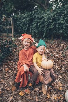 two children sitting on the ground with pumpkins in their hands and one child wearing an elf's hat