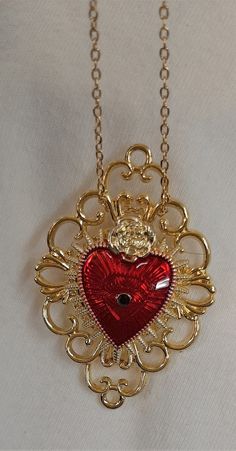 "This goldtone necklace features a lovely mid-sized lacy openwork pendant with a looped outer rim that gives it charm and character.  The center is accented with a gorgeous red finished Sacred heart Inset with a \"stigmata\" in the center.  The top is accented with a goldtone rose, signifying Jesus as The Rose of Sharon.   It has a pebbled finish on the reverse and measures 1 1/2 inches wide and 2 1/4 inches long.  It also includes a brooch fitting to allow it to be taken off the chain and worn Red Neckless, Heart Gem Necklace, Red Jeweled Metal Necklaces, Ornate Gold Necklaces For Valentine's Day, Ornate Gold Necklace For Valentine's Day, Sacred Heart Necklace, Red Heart Pendant Jewelry With Heart Detail, Sacred Heart Jewelry Necklaces, Ornate Red Pendant Jewelry