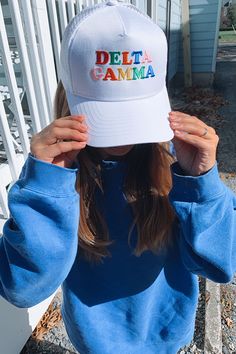 a girl wearing a hat with the word delta gamma on it, covering her eyes