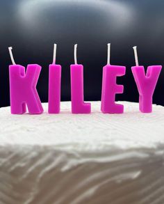 three candles that spell out the word kiley on top of a white frosted cake