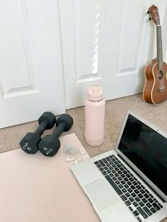 an open laptop computer sitting on top of a floor next to a pair of dumbbells