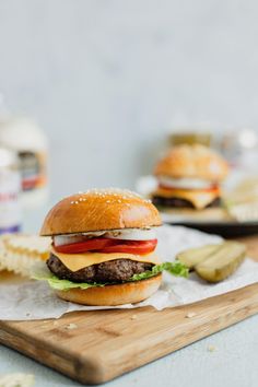 a cheeseburger with lettuce, tomato and pickles on a cutting board