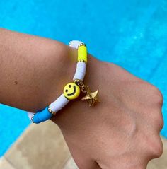 a person wearing a bracelet that has a smiley face on it, next to a swimming pool