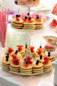 some pancakes and berries are on a table with other desserts in the back ground