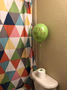 a green balloon sitting on top of a toilet next to a shower curtain in a bathroom