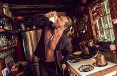 a man drinking from a bottle while standing in a kitchen next to a stove top