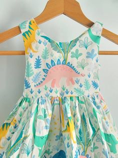 a dress hanging on a wooden hanger in front of a white background with dinosaurs and plants